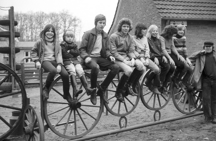 Mehrere Kinder und Jugendliche sitzen auf einem Zaun, neben ihnen steht ein Mann. Foto: Adolf Risse (ca. 1969 - 1979); Archiv für Alltagskultur.